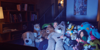 Un homme et une petite fille en face de la télé sur un canapé avec plein de nounours regardent la TV