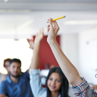 Gros plan de mains levées avec un stylo dans une classe