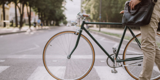 Jeune homme tenant son vélo pour traverser un passage piétons dans la rue